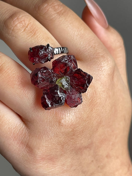 Close-up hand shot of garnet flower ring with peridot center showing raw crystal texture