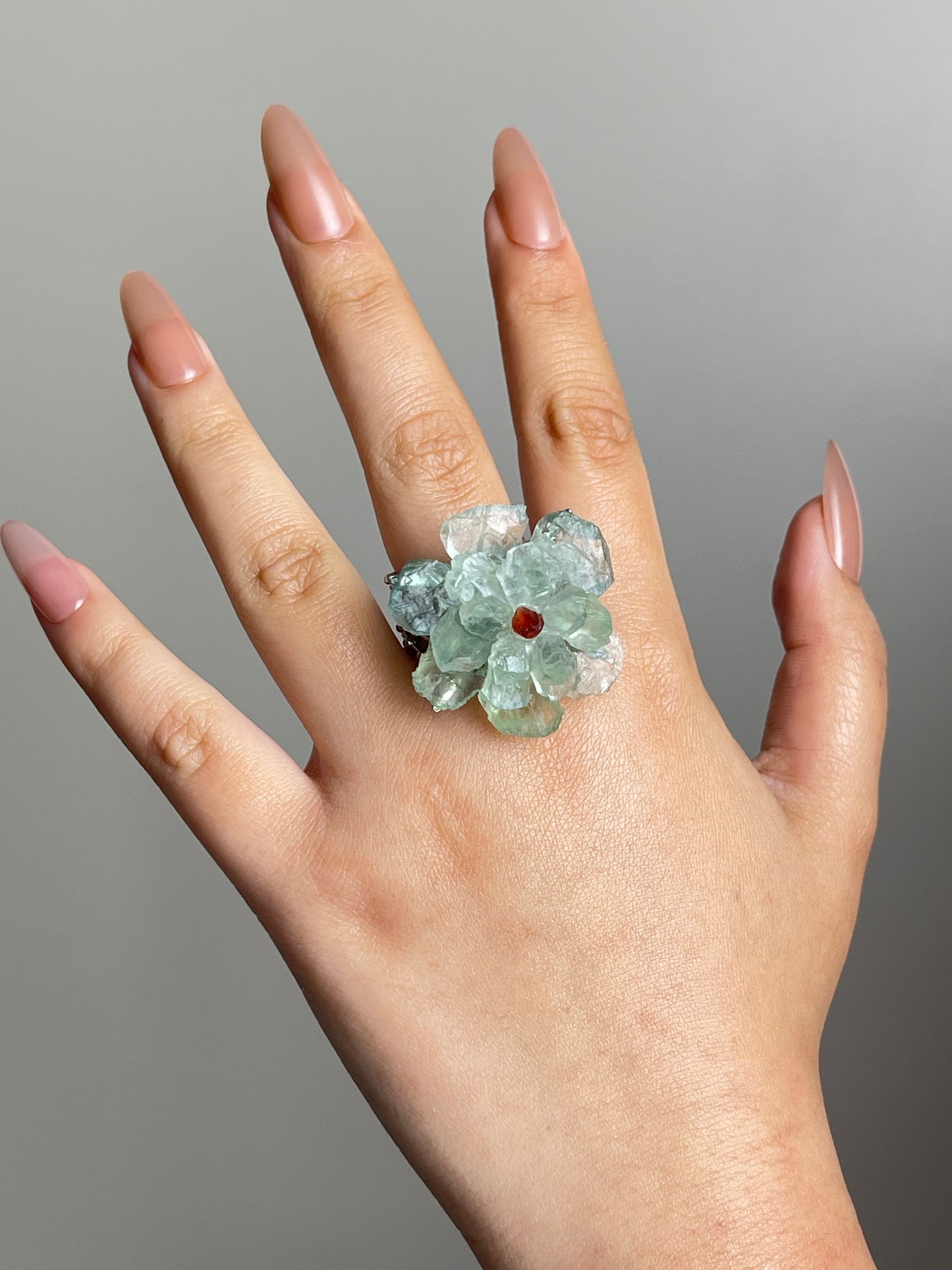 Green quartz flower ring with garnet center worn on hand in gold plated finish