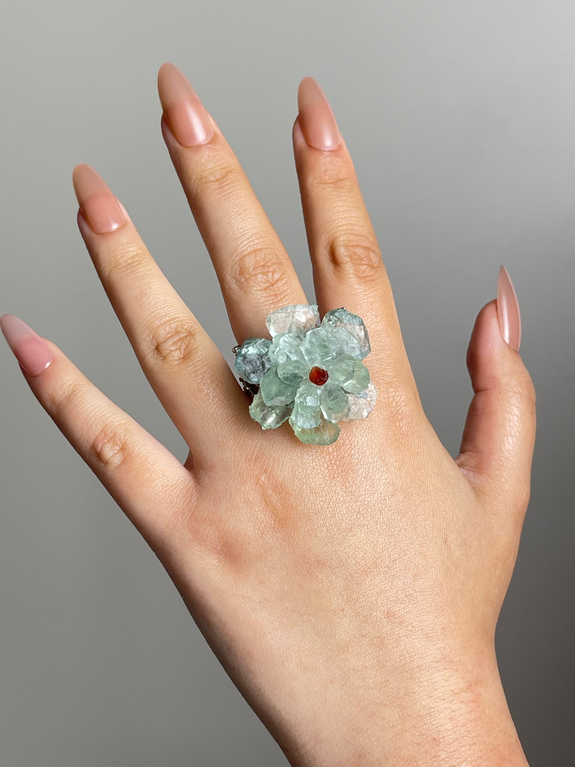 Green quartz flower ring with garnet center worn on hand in gold plated finish