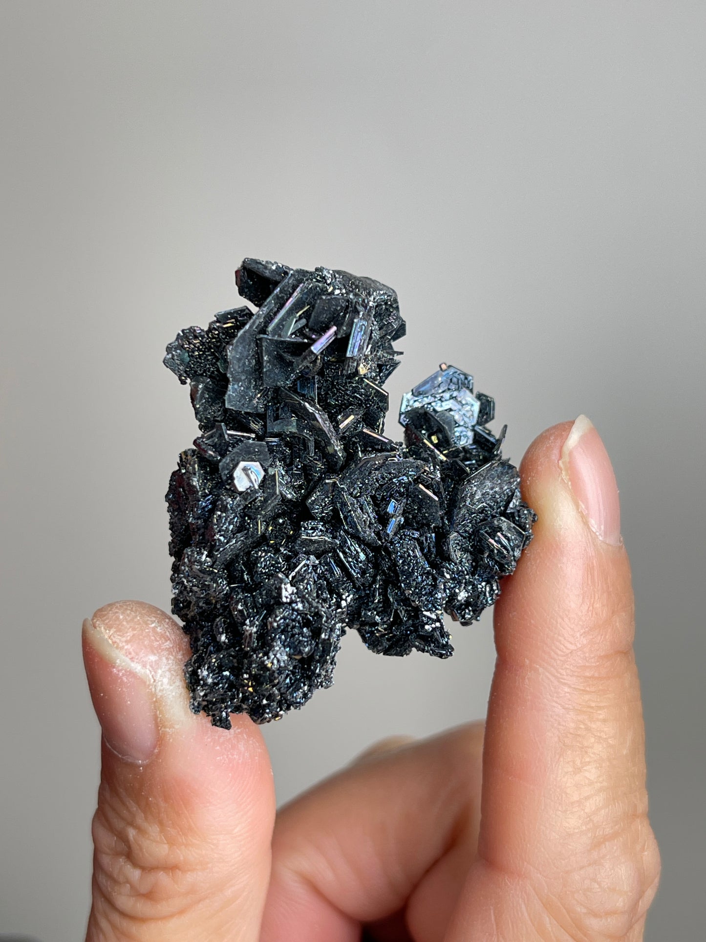 Handheld Rainbow Carborundum cluster mineral specimen showing metallic black crystals and rainbow reflections in close detail.