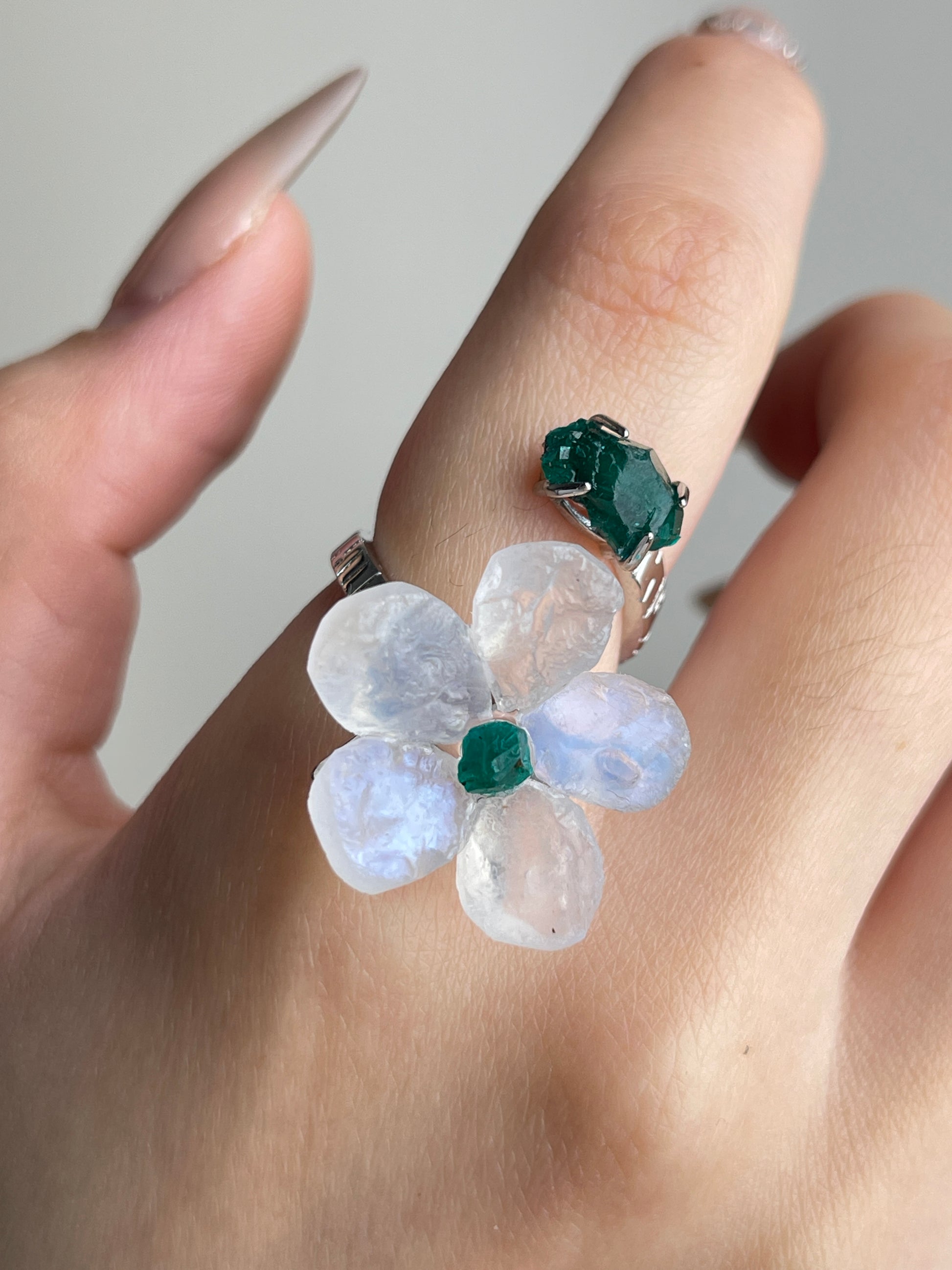 Close-up of Moonstone and Dioptase crystal flower ring worn on hand