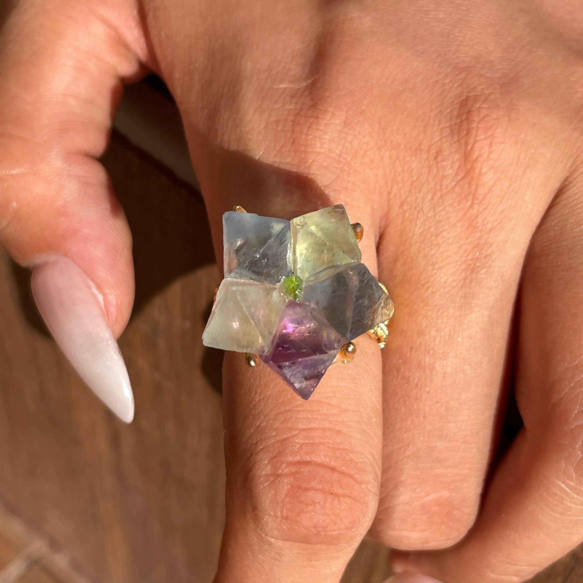 Close-up hand shot of octahedral fluorite flower ring with peridot center showing natural crystal geometry