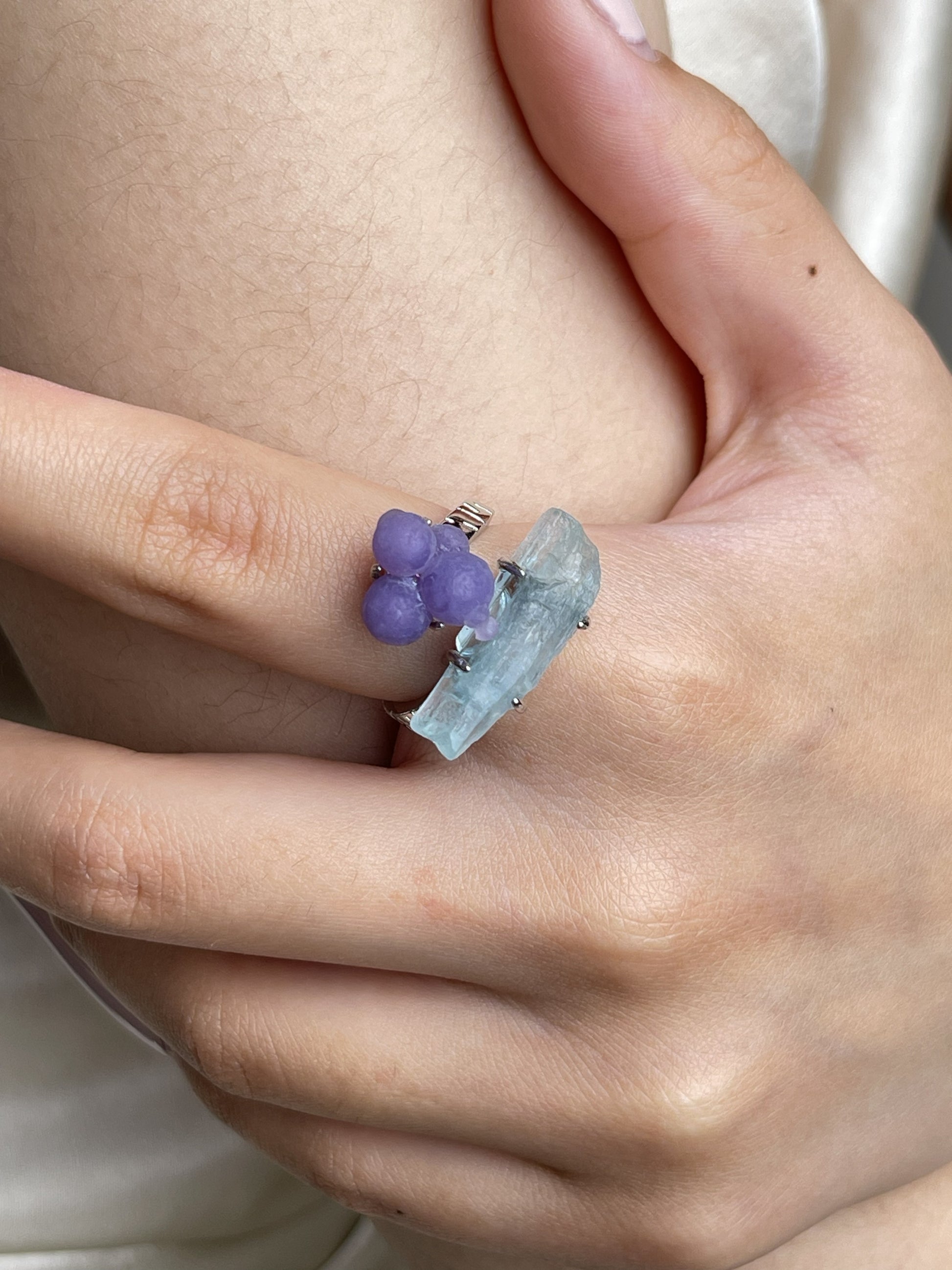 Close-up hand shot of purple grape agate and aquamarine ring showing botryoidal texture and raw blue crystal