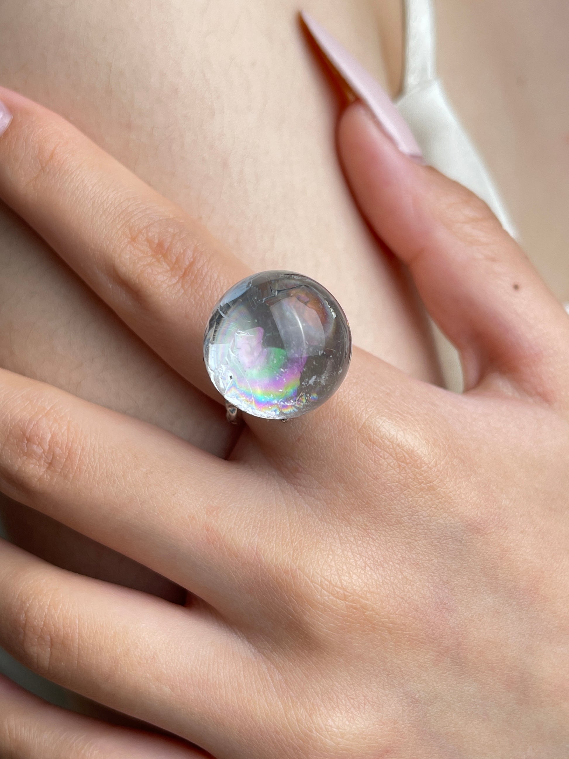 Close up of Rainbow Quartz Sphere ring on hand showing internal rainbow flashes
