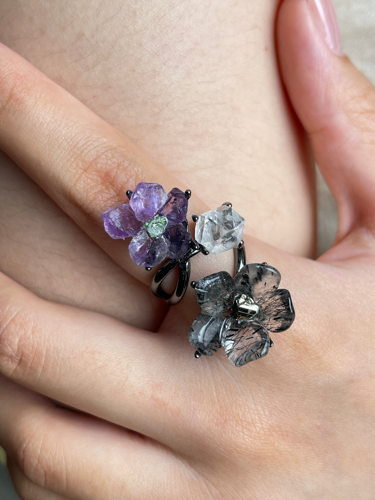 Close up of raw amethyst flower and tourmalinated quartz flower ring with Herkimer Diamond Quartz worn on hand