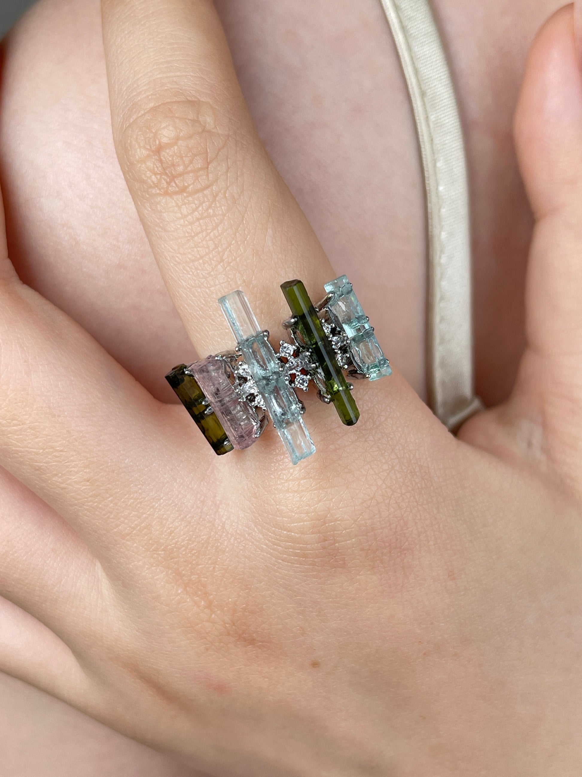 Raw aquamarine, green tourmaline and morganite ring worn on hand, showing colorful natural crystal columns