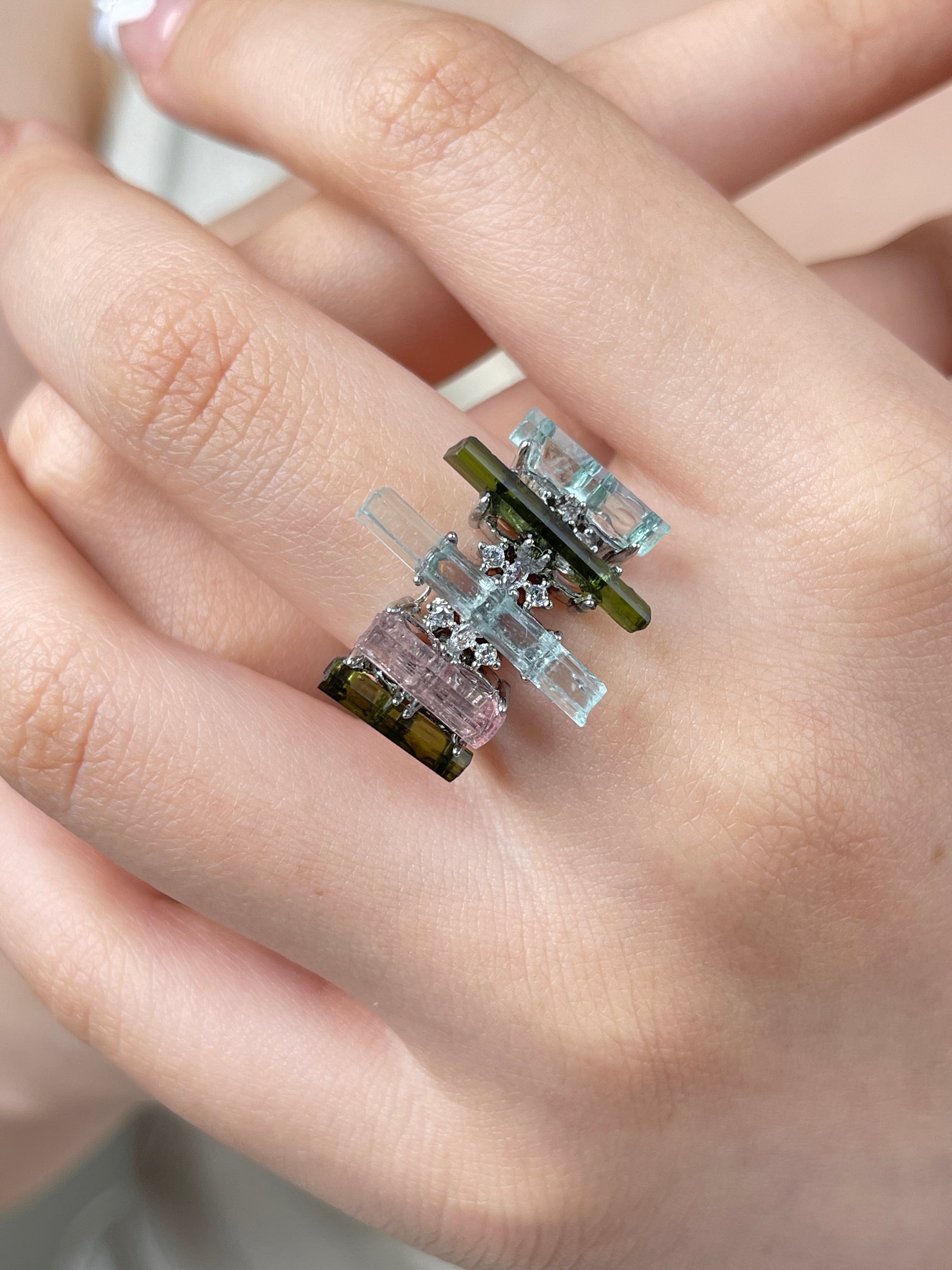 Raw aquamarine, green tourmaline and morganite ring worn on hand, featuring pastel blue, pink and green crystal colors