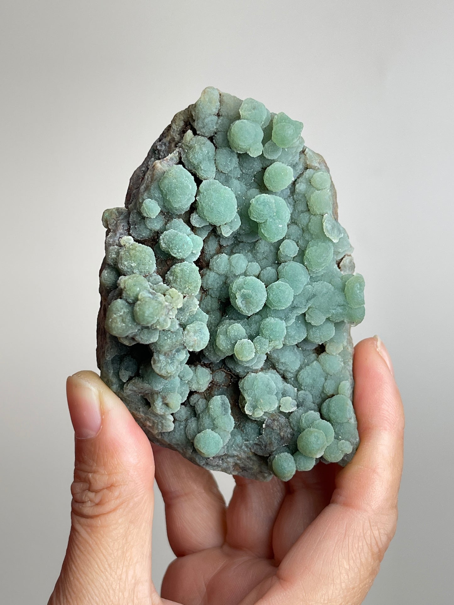 Handheld raw green prehnite mineral specimen showing natural size and texture