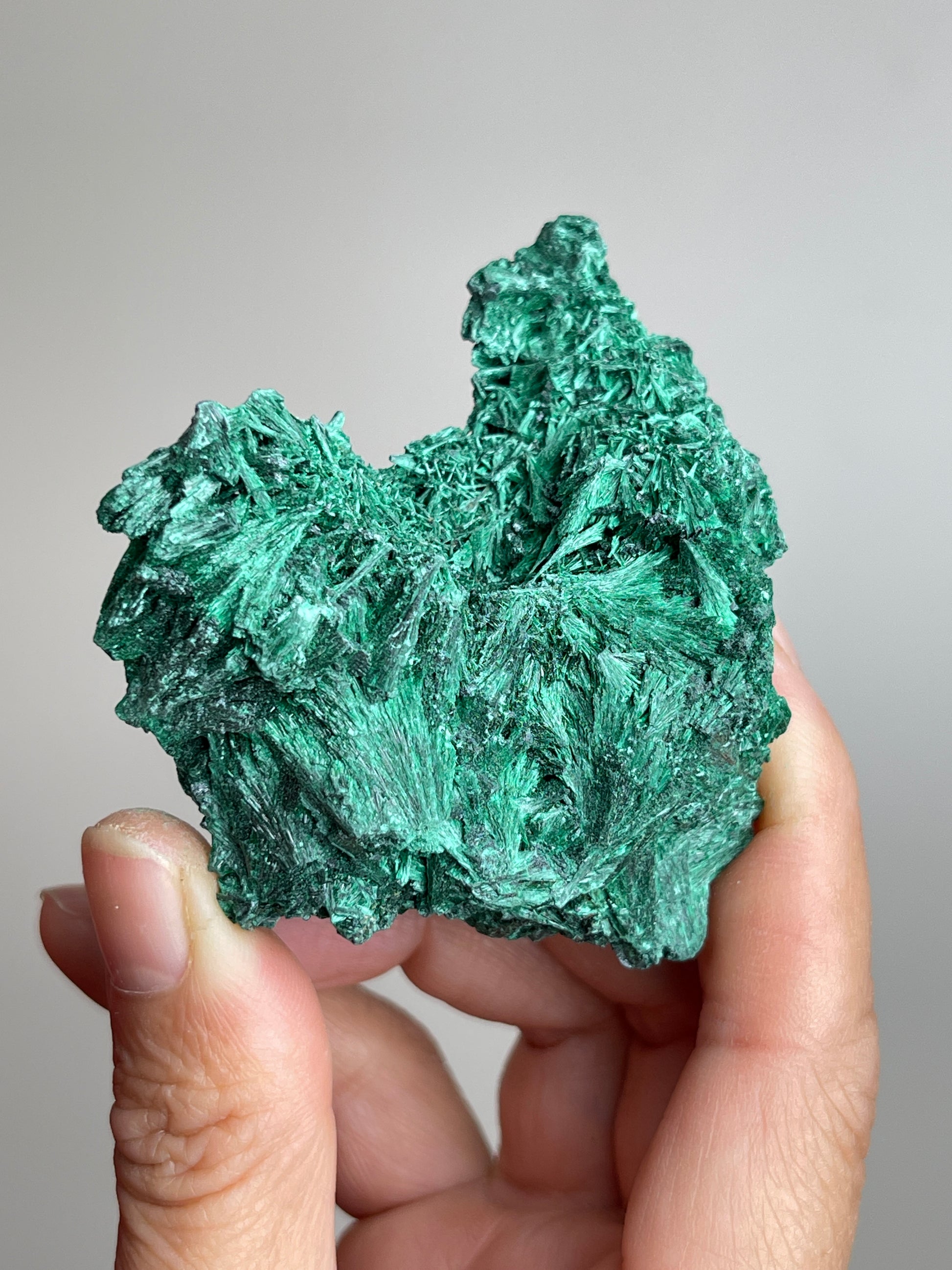 Handheld raw fibrous malachite cluster mineral specimen showing natural size and texture