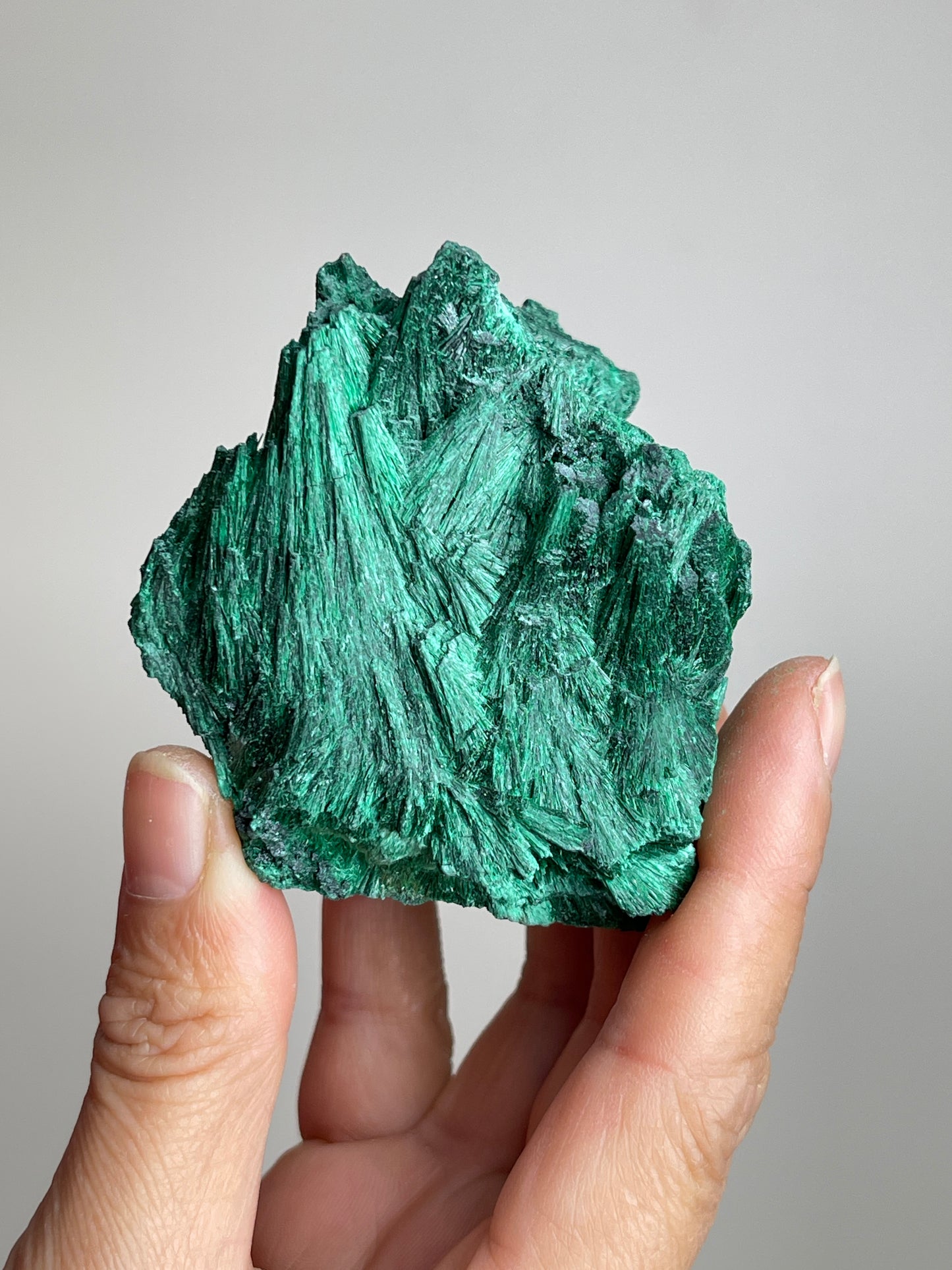 Handheld raw fibrous malachite fan cluster mineral specimen showing natural size and texture