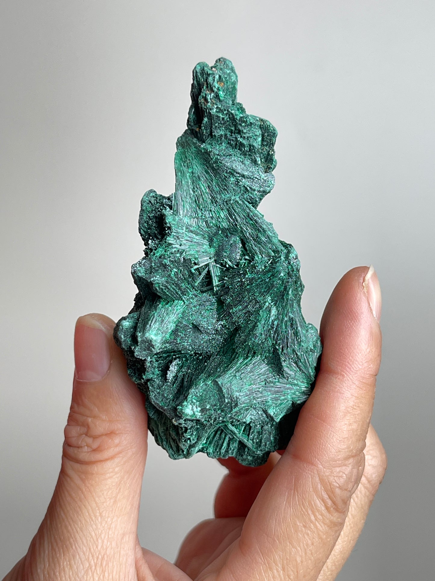 Handheld raw fibrous malachite mineral specimen showing natural size and texture