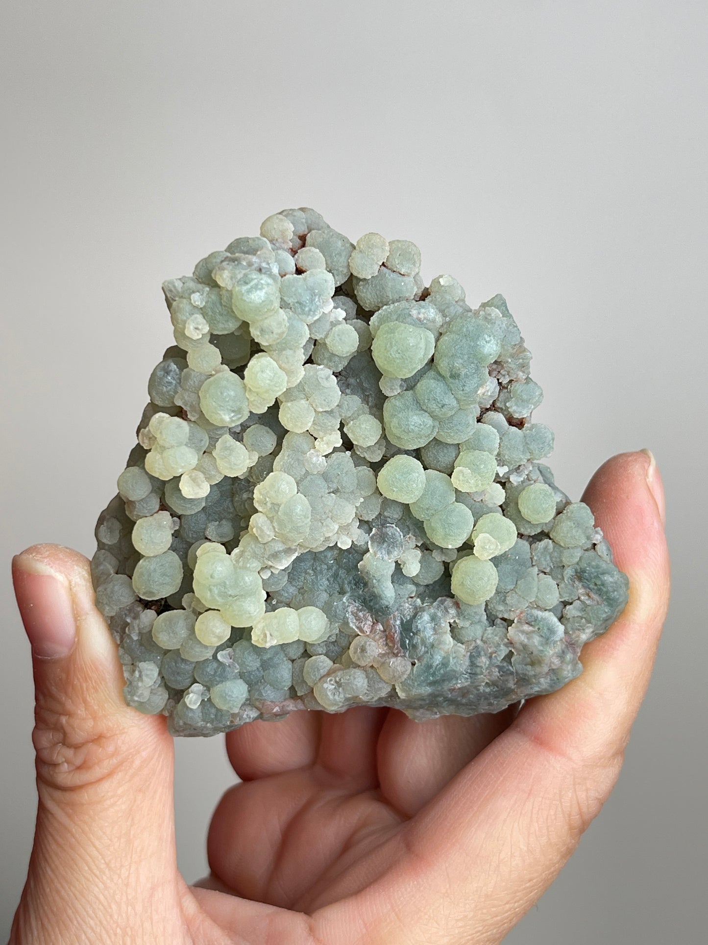 Handheld raw green prehnite mineral specimen from Morocco showing natural size and texture