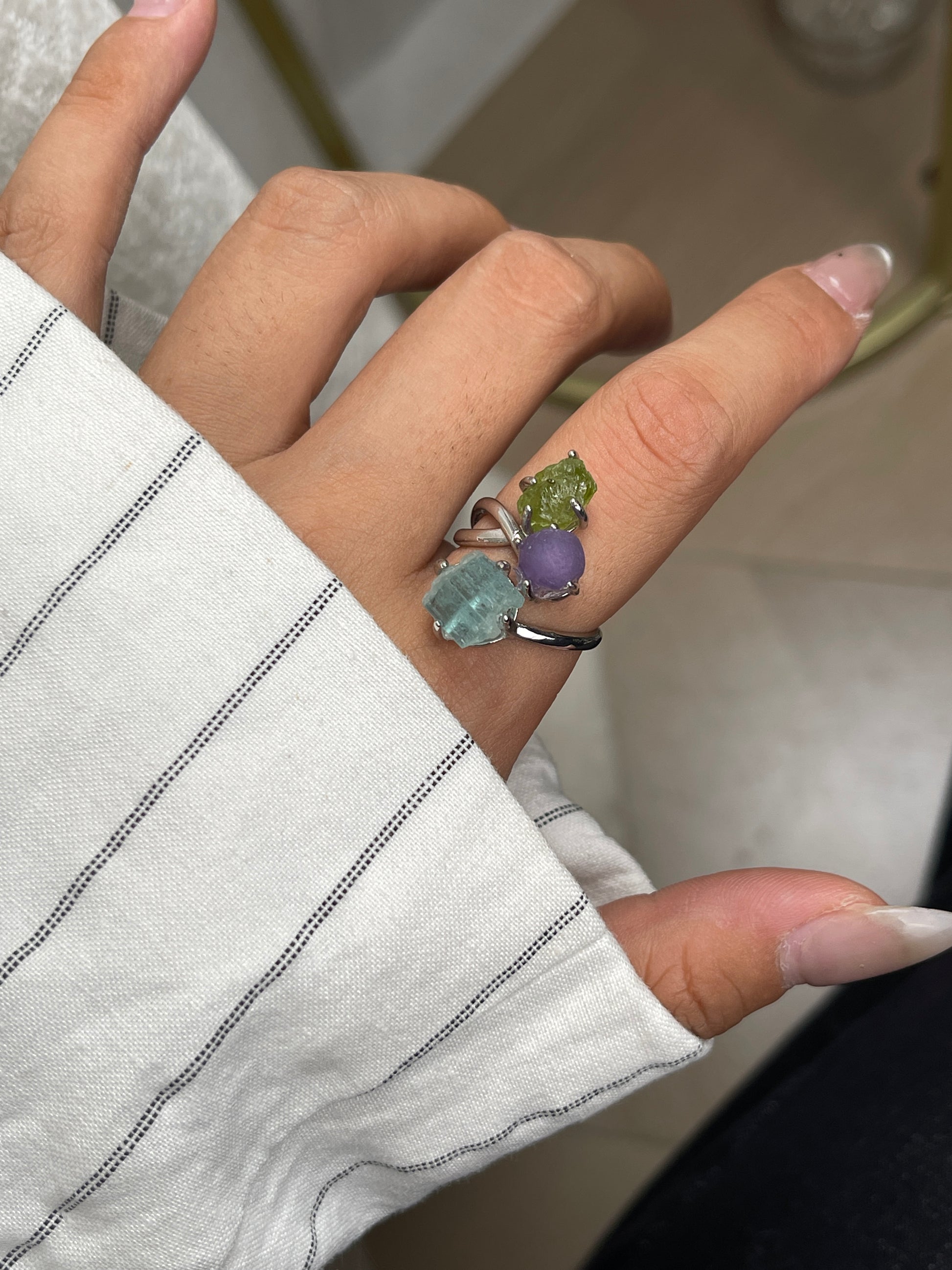 Close up of raw peridot, purple grape agate and raw aquamarine ring worn on hand
