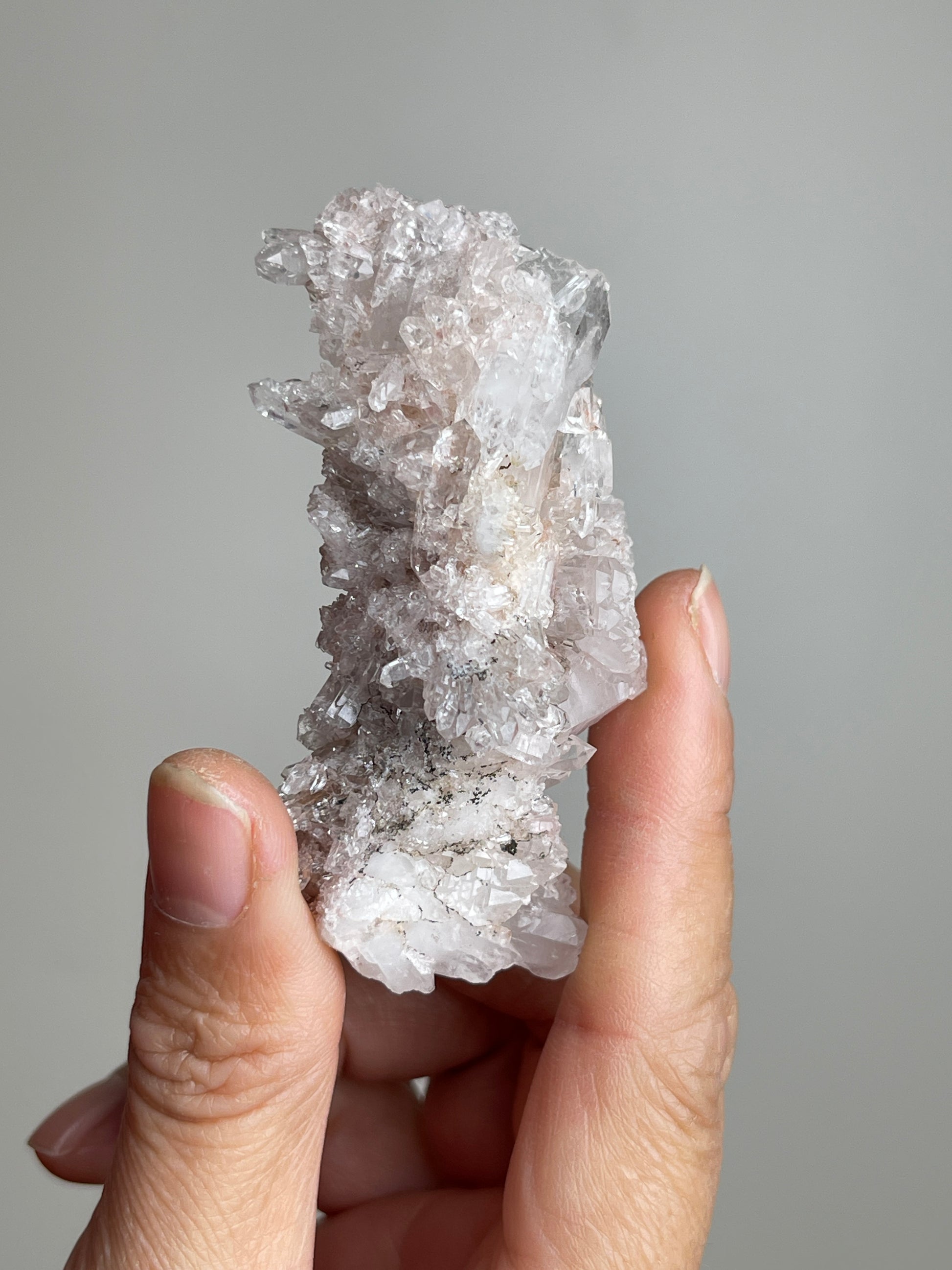 Handheld Pink Lemurian Quartz cluster with manganese oxides showing natural size and crystal form